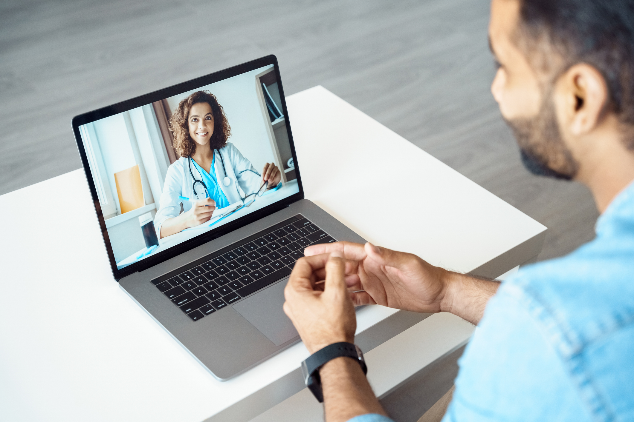 View over male client shoulder sit at desk receive medical consultation online from female doctor. Indian man listening practitioner. Distant communication, health protection and telemedicine concept